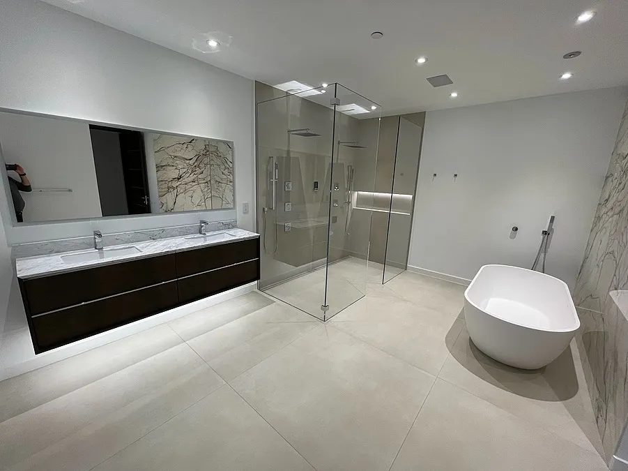 Modern bathroom with a dark wood double vanity, a glass shower, and a white freestanding tub on light tiled floor.