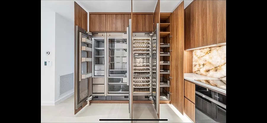 Modern kitchen with open built-in refrigerator, freezer, wine cooler, pantry, oven, and backlit marble backsplash.