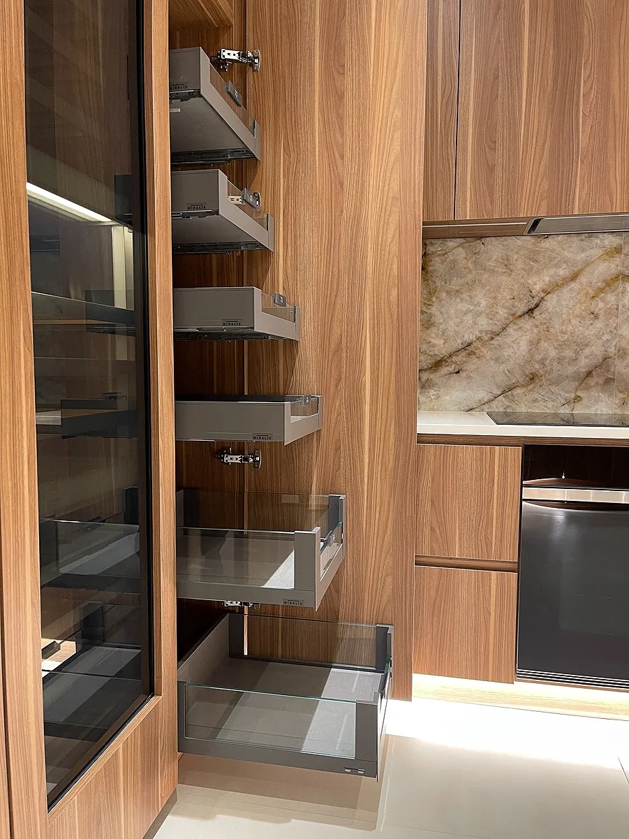 Pull-out pantry drawers with glass sides in a modern wooden kitchen cabinet, next to a marbled countertop.