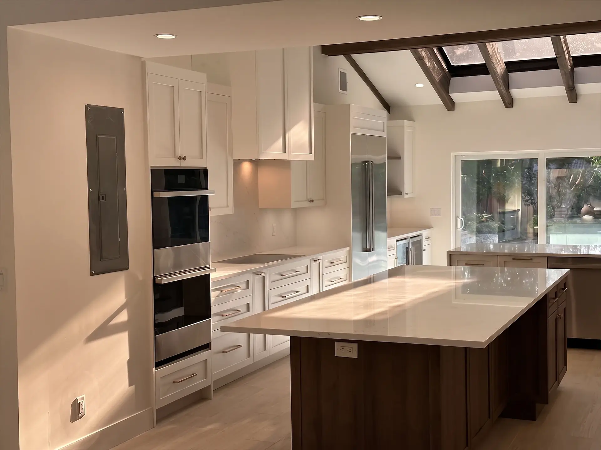 Modern kitchen with white cabinets, dark wood island, stainless steel appliances, wood floor, and skylight.