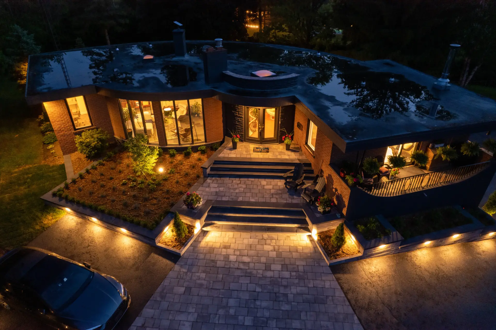 Modern curved house illuminated at night, with warm lights highlighting its unique architecture, landscaping, and driveway.