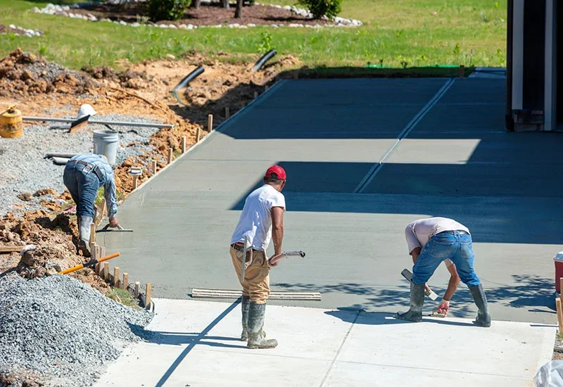 Three construction workers pour and smooth a new concrete driveway.