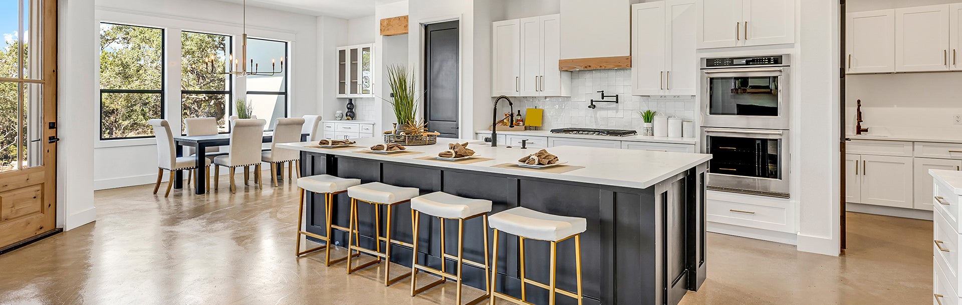 Modern open-concept kitchen with a dark island, white countertops, stainless appliances, and a dining area with large windows.